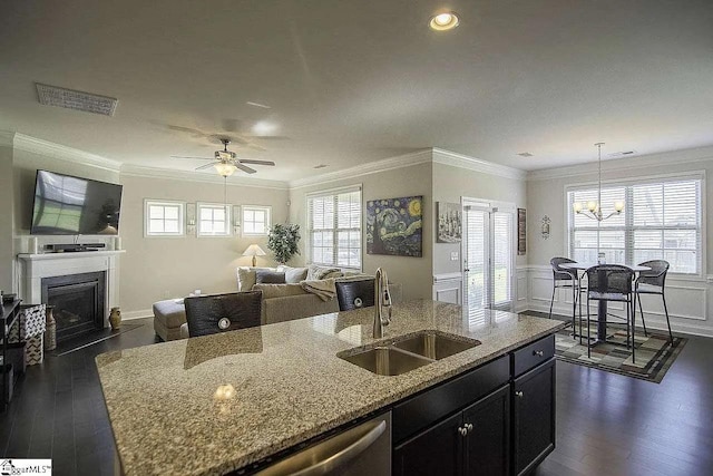 kitchen featuring a fireplace with flush hearth, a kitchen island with sink, a sink, open floor plan, and light stone countertops