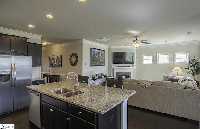 kitchen featuring an island with sink, a sink, a glass covered fireplace, open floor plan, and appliances with stainless steel finishes