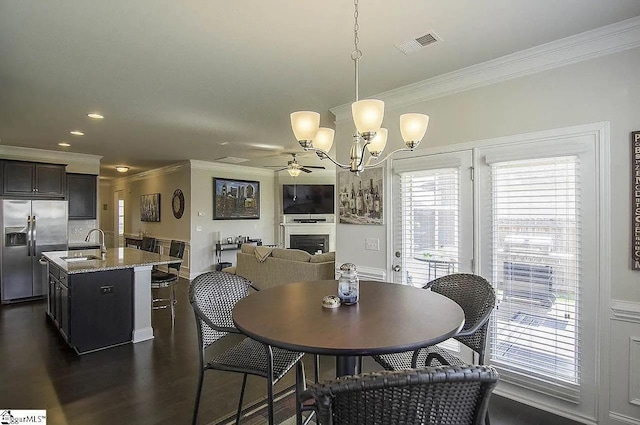 dining space featuring visible vents, ceiling fan with notable chandelier, crown molding, a fireplace, and dark wood-style flooring