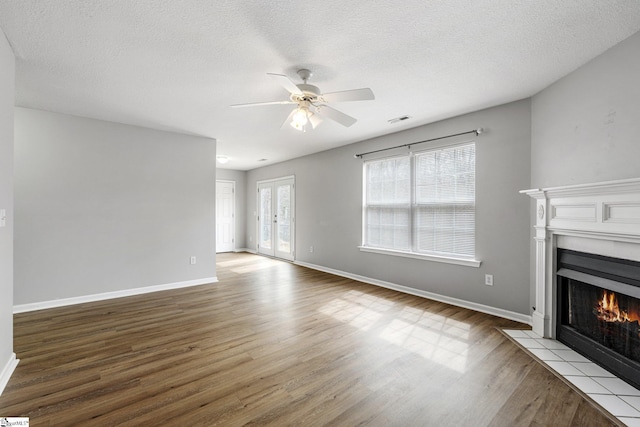 unfurnished living room featuring a fireplace with flush hearth, visible vents, baseboards, and wood finished floors