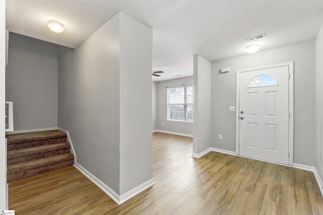 entryway with light wood finished floors, stairway, visible vents, and baseboards