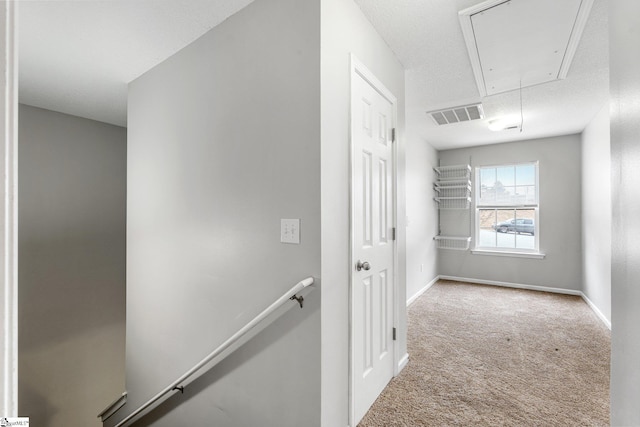 hallway with carpet, visible vents, attic access, an upstairs landing, and baseboards