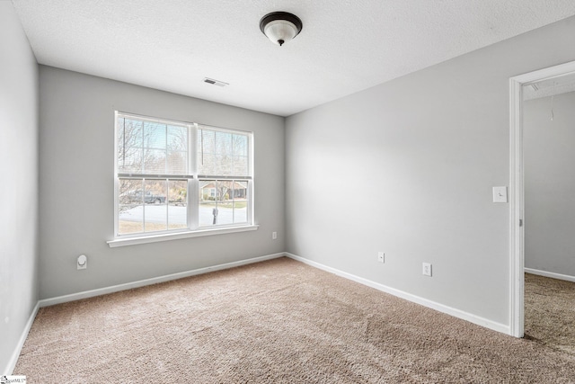 carpeted empty room featuring attic access, a textured ceiling, visible vents, and baseboards