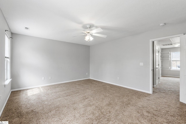 spare room featuring carpet flooring, visible vents, baseboards, a ceiling fan, and attic access