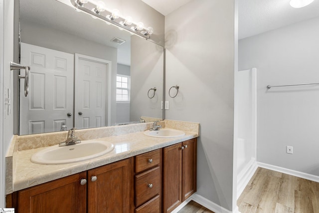 bathroom featuring double vanity, wood finished floors, a sink, and visible vents