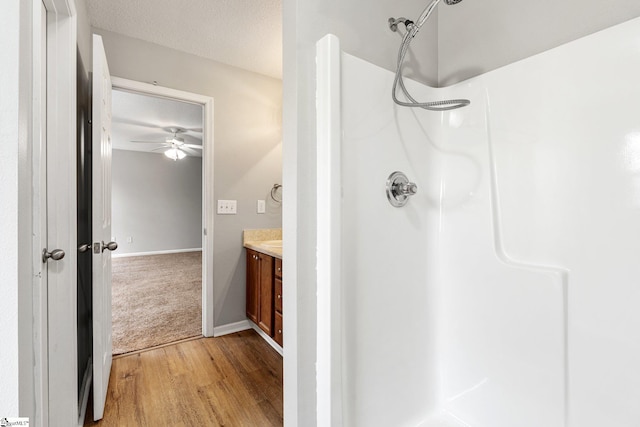 bathroom featuring baseboards, wood finished floors, walk in shower, a textured ceiling, and vanity