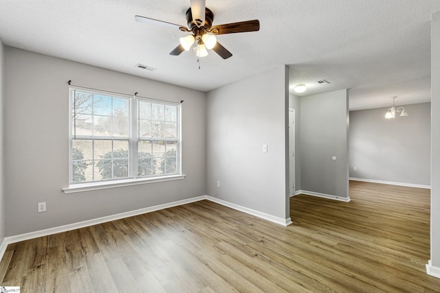 spare room with baseboards, visible vents, wood finished floors, and ceiling fan with notable chandelier