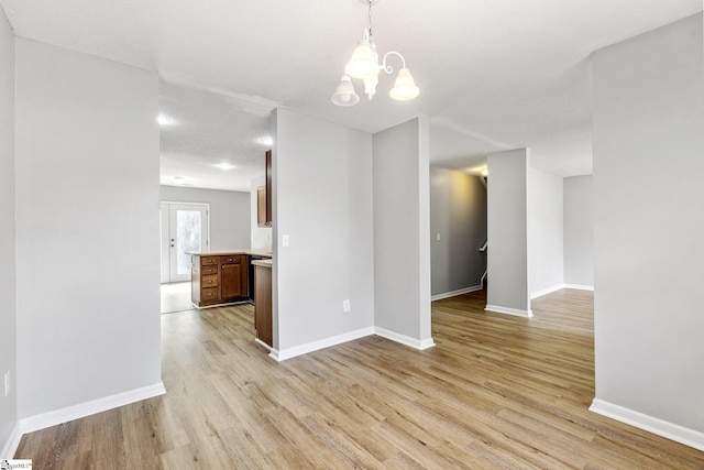 unfurnished room featuring an inviting chandelier, light wood-style flooring, and baseboards