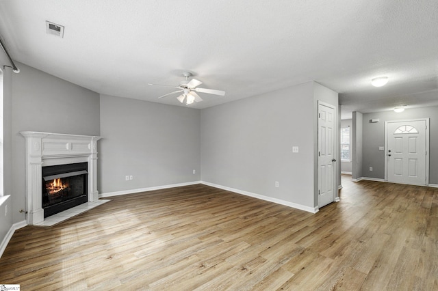 unfurnished living room featuring visible vents, ceiling fan, a fireplace with flush hearth, light wood-style flooring, and a textured ceiling