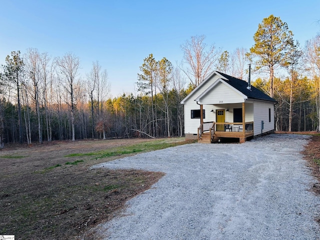 view of front of house with a porch, crawl space, driveway, and a view of trees