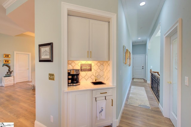 corridor featuring recessed lighting, a sink, baseboards, light wood-style floors, and ornamental molding