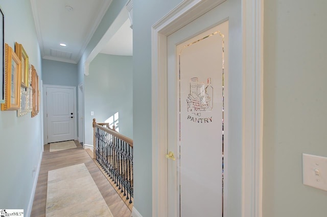 hallway featuring light wood-style flooring, visible vents, an upstairs landing, baseboards, and ornamental molding