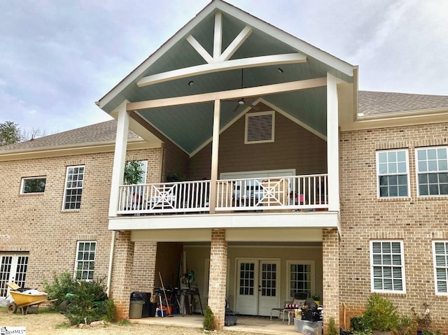 back of property featuring french doors, roof with shingles, a balcony, and brick siding