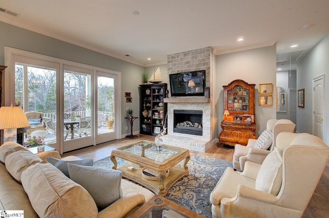 living room with a large fireplace, attic access, visible vents, ornamental molding, and wood finished floors