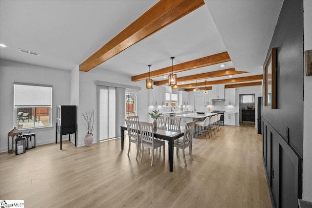 dining room featuring light wood-type flooring, plenty of natural light, visible vents, and beamed ceiling