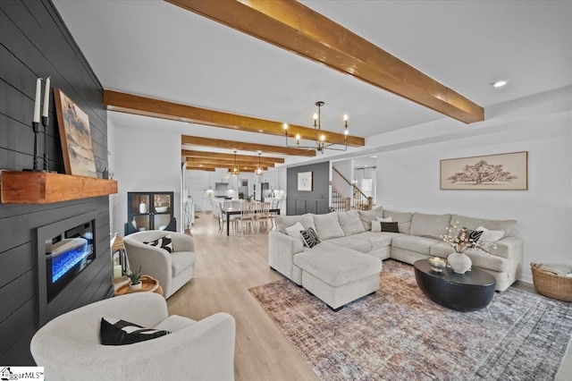 living room featuring beam ceiling, light wood-style flooring, a large fireplace, a chandelier, and stairs