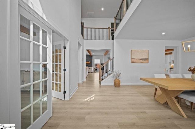 entryway featuring wood finished floors, a towering ceiling, visible vents, stairs, and baseboards