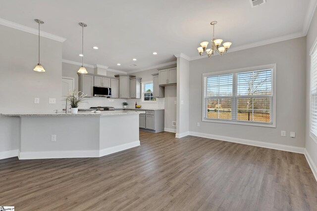 kitchen featuring tasteful backsplash, gray cabinets, stainless steel microwave, wood finished floors, and a peninsula