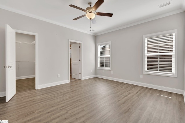 unfurnished bedroom featuring visible vents, a walk in closet, wood finished floors, and ornamental molding