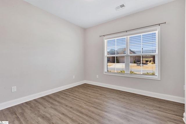 spare room featuring wood finished floors, visible vents, and baseboards