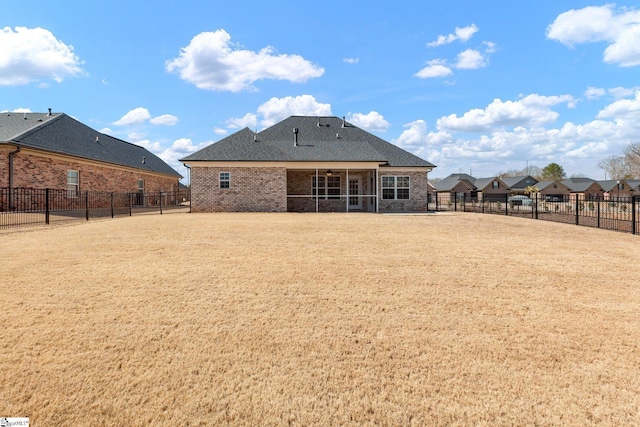 rear view of property with a shingled roof, a ceiling fan, a sunroom, a fenced backyard, and brick siding