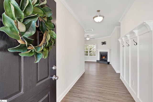 foyer with wood finished floors, a ceiling fan, visible vents, a glass covered fireplace, and crown molding