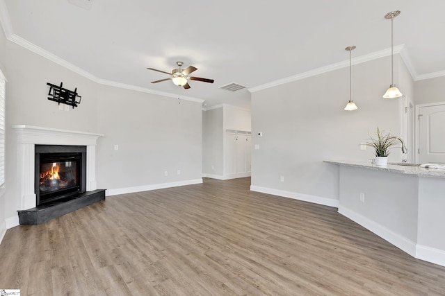 unfurnished living room with wood finished floors, visible vents, baseboards, a glass covered fireplace, and crown molding