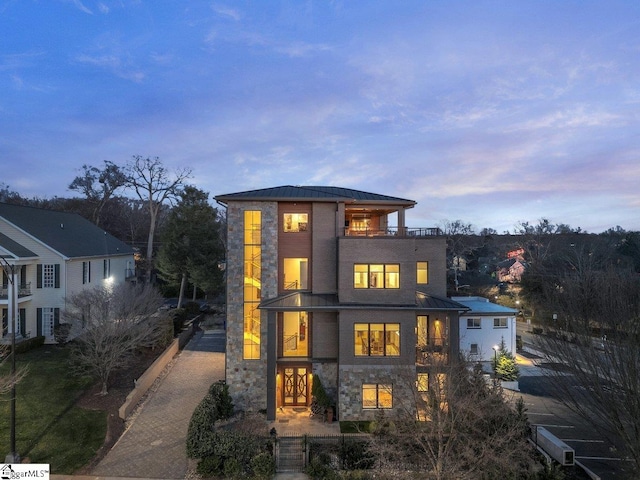 back of house with a balcony, stone siding, metal roof, a standing seam roof, and decorative driveway