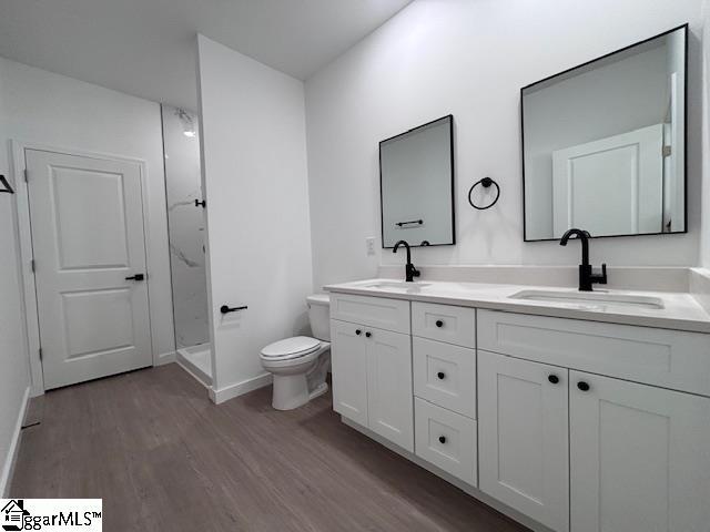 full bathroom with double vanity, toilet, a sink, and wood finished floors