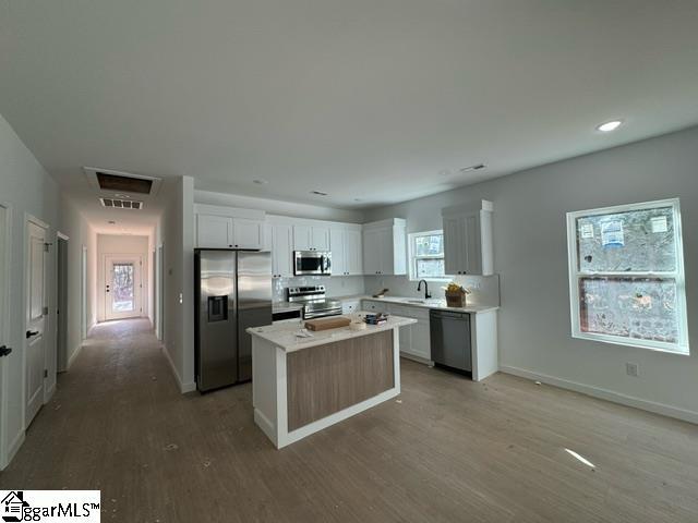 kitchen featuring stainless steel appliances, a kitchen island, white cabinetry, light countertops, and light wood-type flooring