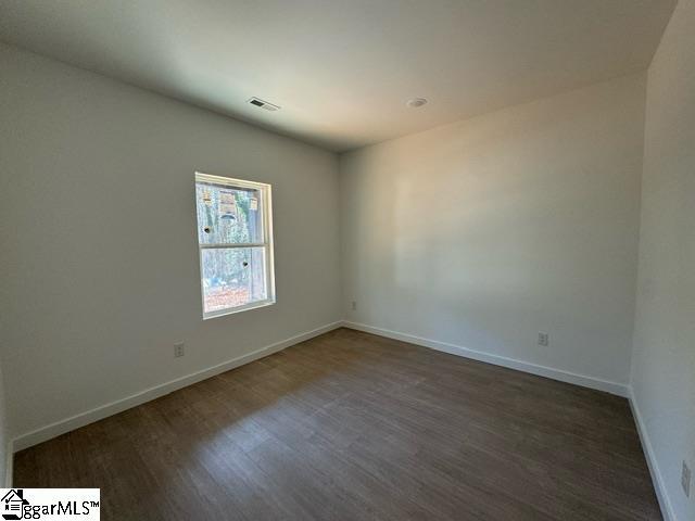 unfurnished room featuring visible vents, dark wood finished floors, and baseboards