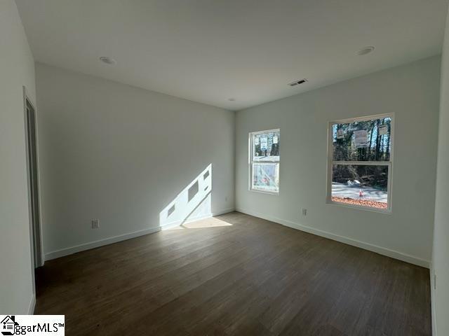 empty room featuring visible vents, dark wood finished floors, and baseboards