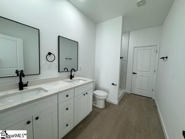 full bath featuring double vanity, a sink, toilet, and wood finished floors