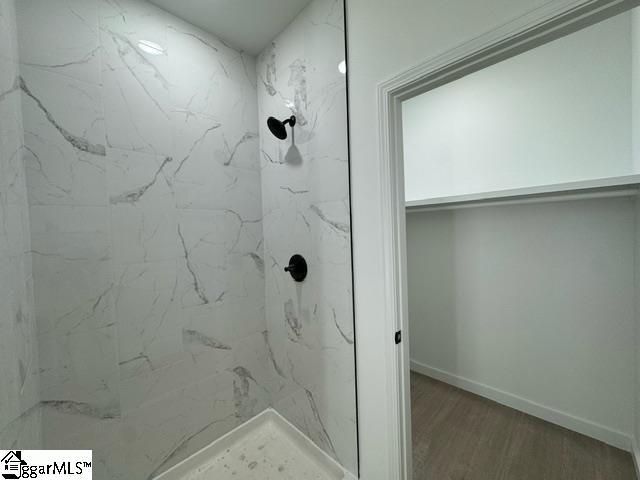 full bathroom featuring baseboards, a marble finish shower, and wood finished floors