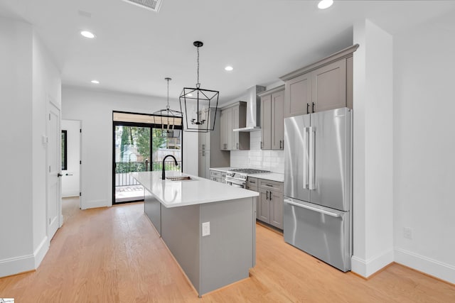 kitchen with gray cabinets, light wood-style flooring, appliances with stainless steel finishes, a sink, and wall chimney range hood