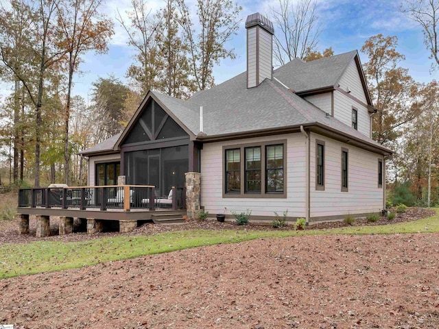 back of property with a sunroom, roof with shingles, a chimney, and a wooden deck