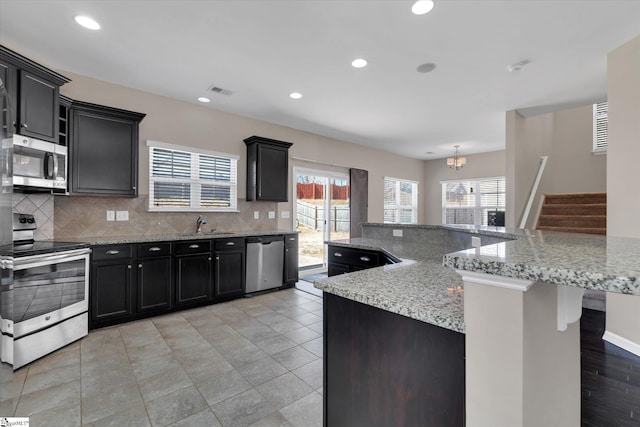 kitchen with a healthy amount of sunlight, tasteful backsplash, stainless steel appliances, and dark cabinetry