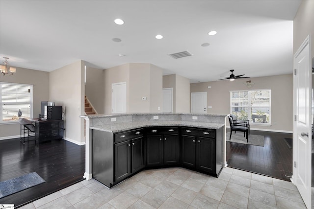 kitchen featuring visible vents, a kitchen island, light stone counters, dark cabinets, and recessed lighting