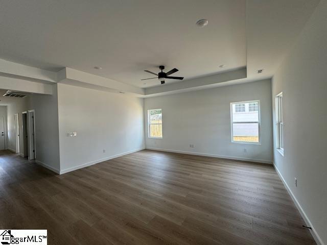 empty room featuring dark wood-style flooring, a raised ceiling, visible vents, and baseboards