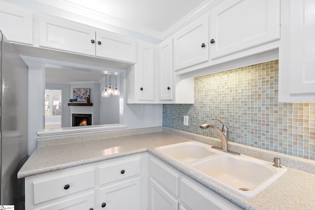 kitchen with crown molding, light countertops, white cabinetry, a sink, and a warm lit fireplace