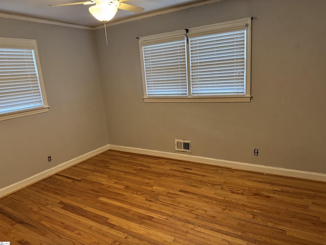 empty room featuring visible vents, wood finished floors, crown molding, baseboards, and ceiling fan