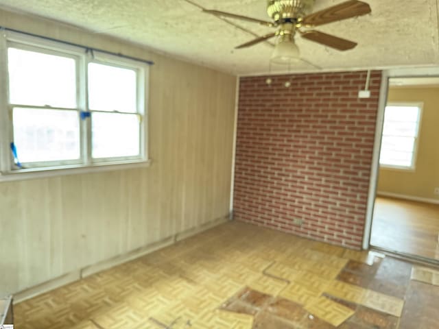 unfurnished room with brick wall, parquet flooring, wood walls, a textured ceiling, and a ceiling fan