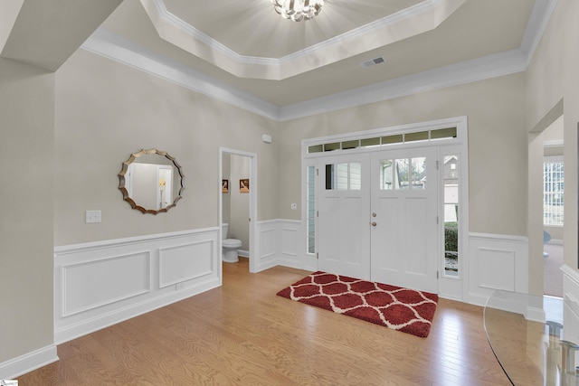 entrance foyer featuring a raised ceiling, crown molding, wood finished floors, and visible vents