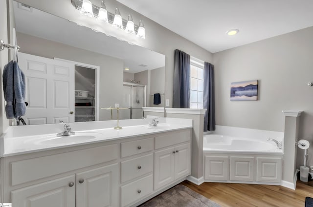 bathroom with a garden tub, a sink, wood finished floors, a shower stall, and double vanity