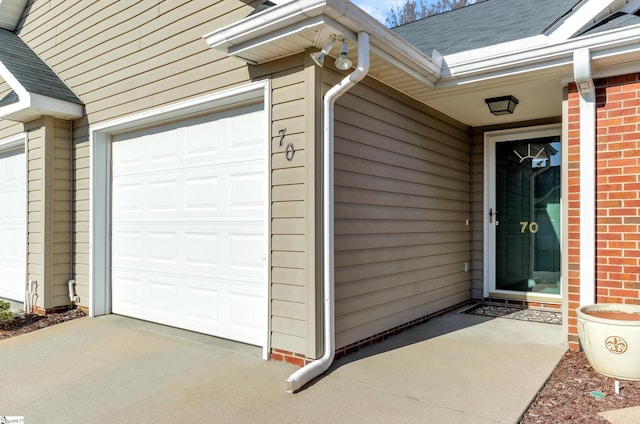 doorway to property with a garage, brick siding, and roof with shingles