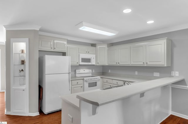 kitchen with a breakfast bar, a sink, dark wood finished floors, white appliances, and a peninsula