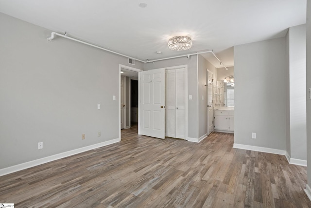 unfurnished bedroom featuring baseboards, an inviting chandelier, wood finished floors, and ensuite bathroom