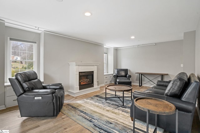 living area featuring recessed lighting, a fireplace with raised hearth, baseboards, and light wood-style floors