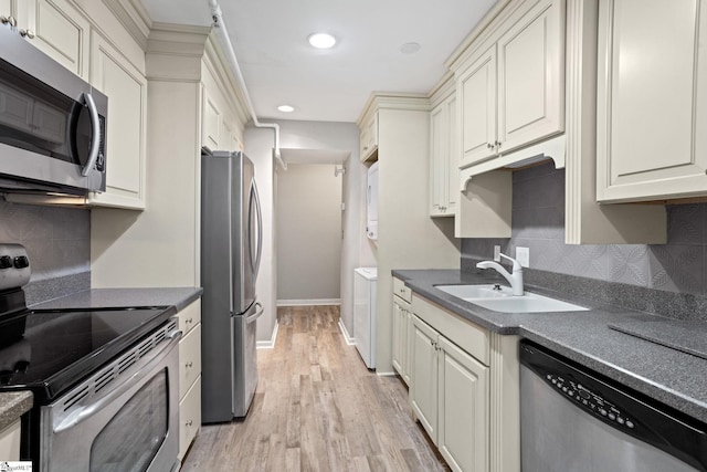 kitchen featuring light wood finished floors, baseboards, decorative backsplash, appliances with stainless steel finishes, and a sink