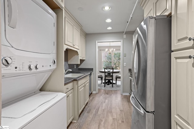 laundry area featuring light wood-type flooring, stacked washer and clothes dryer, a sink, recessed lighting, and an inviting chandelier